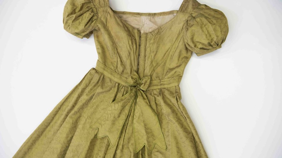 Fotografie zadního dílu dámských hedvábných šatů. Ručně šité s balonkovými rukávy, pas zvýšený, podšívka živůtku vyztužená kosticemi, období empiru, kolem roku 1810 | foto: Národopisné muzeum Plzeňska / Západočeské muzeum v Plzni Fotografie zadního dílu dámských hedvábných šatů. Ručně šité s balonkovými rukávy, pas zvýšený, podšívka živůtku vyztužená kosticemi, období empiru, kolem roku 1810